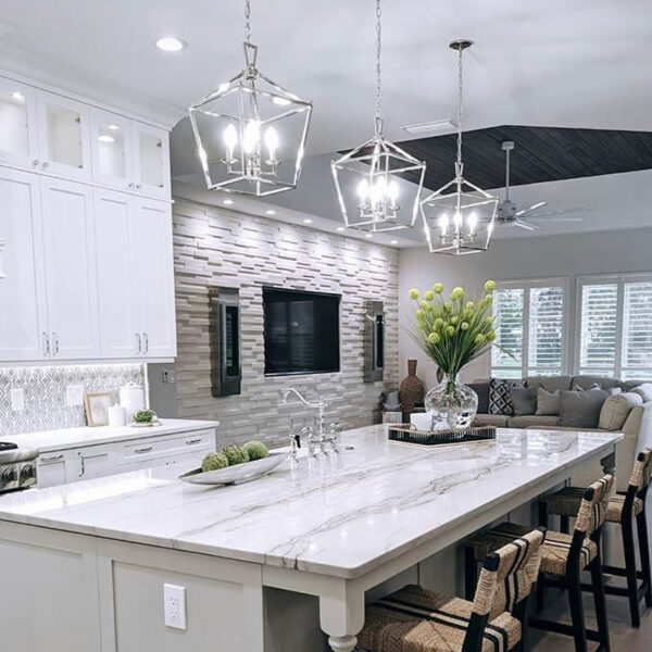 A kitchen with pendant lighting, recessed lights, and under cabinet lighting. A large TV setup is mounted in the adjoined den.
