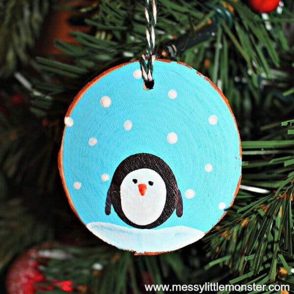 Ornament featuring a penguin on a wood slice ornament hanging from a Christmas tree