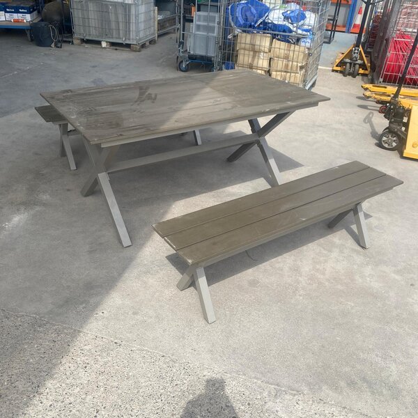 Mesa de jardín con bancos y superficie de lamas oscuras.