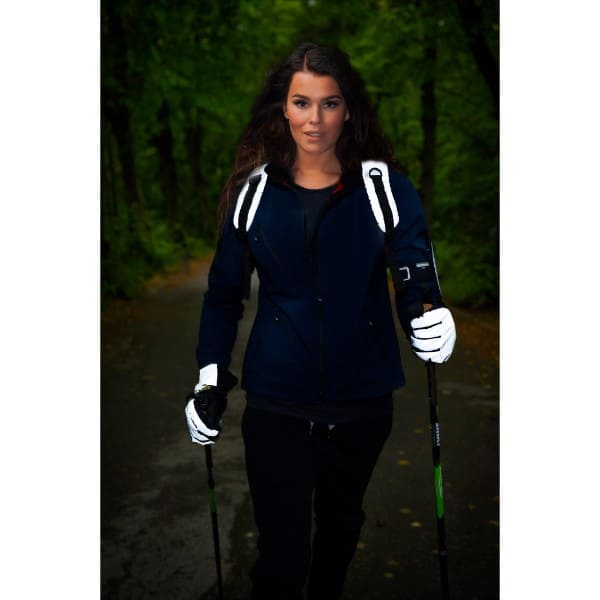 Nainen sauvakävelee. Hänellä on Huomio heijastinhanskat ja heijastava reppu selässä.