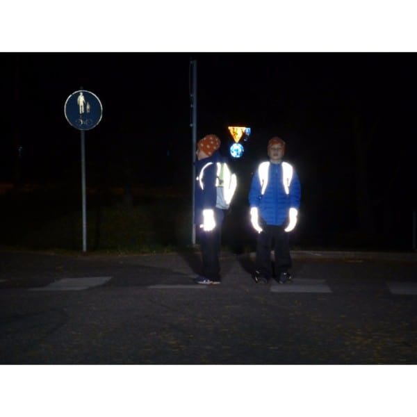 Kaksi lasta pimeällä suojatiellä. Selässä heijastavat reput ja käsissä heijastavat toppahanskat. Hyvin näkyvät pimeällä.