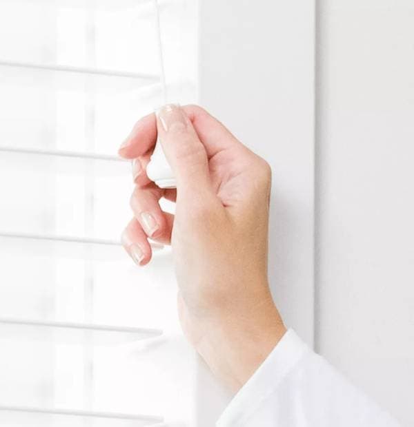 Close-up of hand adjusting white window blinds, bright interior lighting, modern home decor.