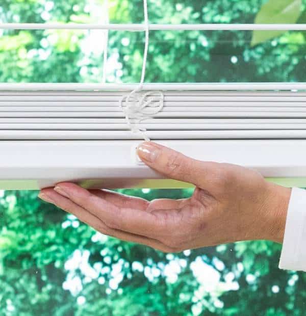 Close-up of a hand fixing a window blind cord.