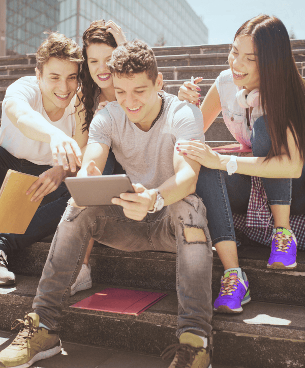 Eine Gruppe junger Menschen sitzt auf einer Treppe. Im Vordergrund schaut ein junger Mann gut gelaunt auf sein Smartphone, während andere Personen hinter ihm ebenfalls interessiert und freundlich in die Richtung blicken.