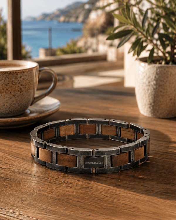 Bracelet homme en bois et métal Zwood® posé sur une table en bois, ambiance terrasse café en bord de mer.