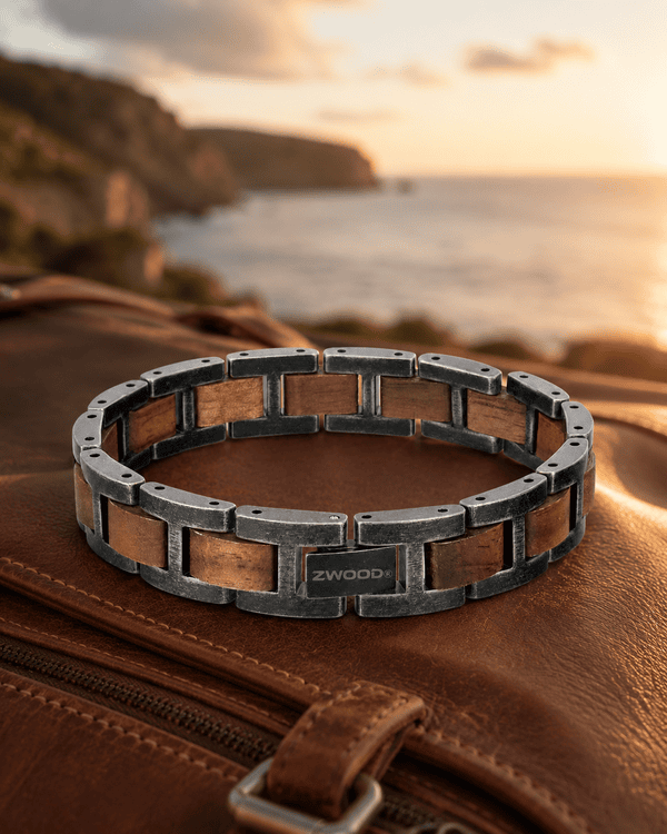 Bracelet homme en bois et métal Zwood® posé sur un sac en cuir, ambiance voyage au coucher du soleil.