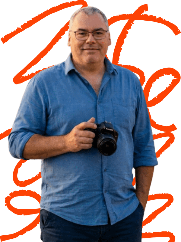 Portrait de Franck Laforest tenant un appareil photo devant un fond graphique orange.