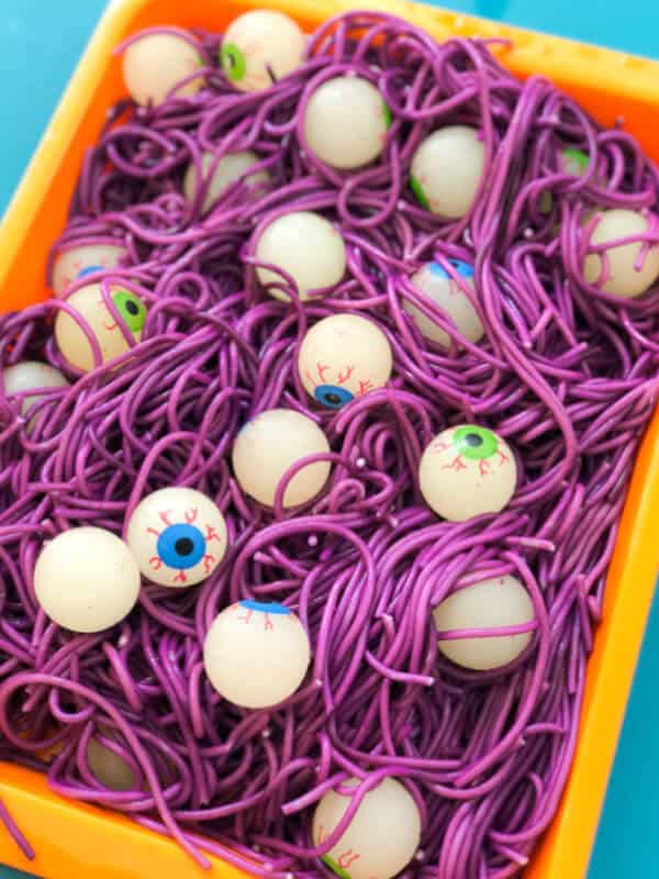 Halloween-themed sensory bin with purple spaghetti and spooky toy eyeballs