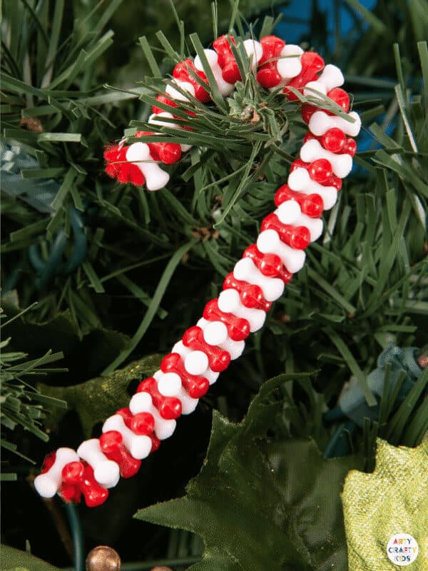 White and red beaded candy cane ornament hanging from Christmas tree