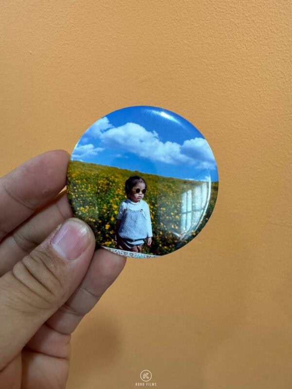 Round photo magnet of a child in a flower field, held in a hand