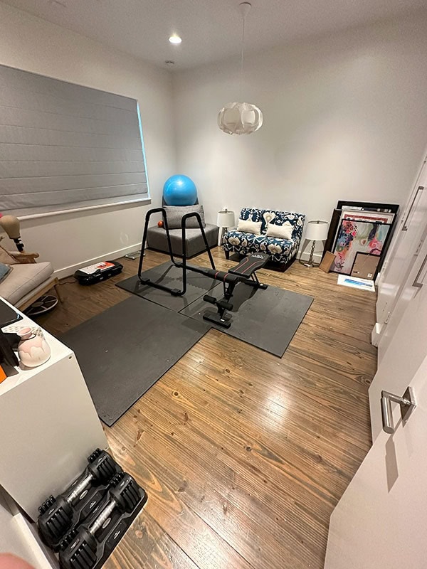 Home gym workout space with exercise equipment, stability ball, and cozy seating area in a bright, modern room featuring hardwood floors and minimalist decor for wellness and relaxation.