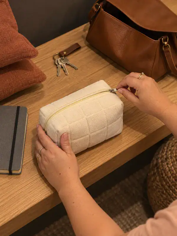 Manos abriendo un neceser junto a un bolso y unas llaves