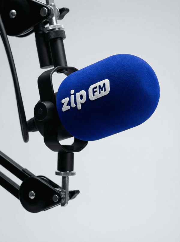 Blue foam microphone windscreen with embroidered ZIP FM logo on a studio broadcast microphone mounted on a boom arm.