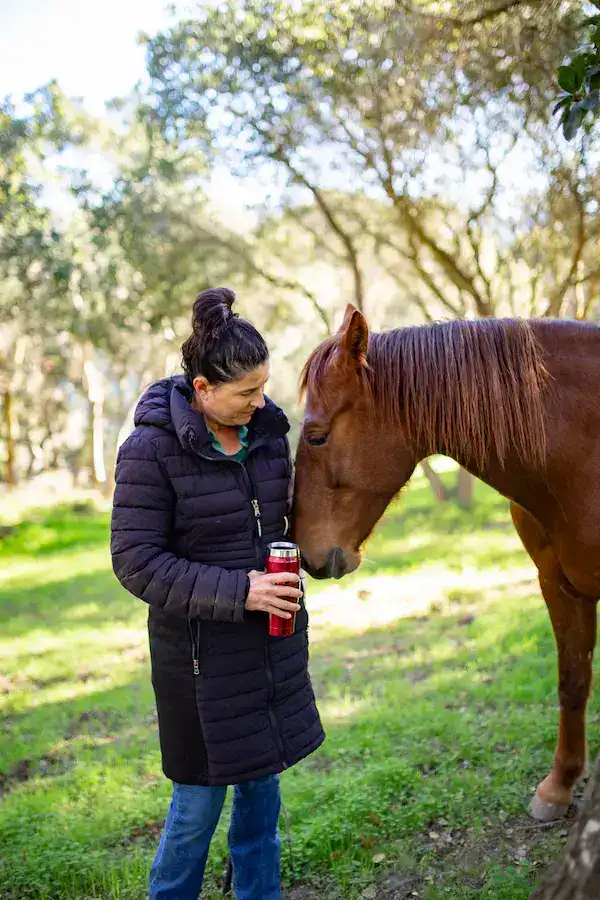 Angel Batt sharing a quiet moment with a horse in a wooded outdoor sanctuary at Beyond Liberty