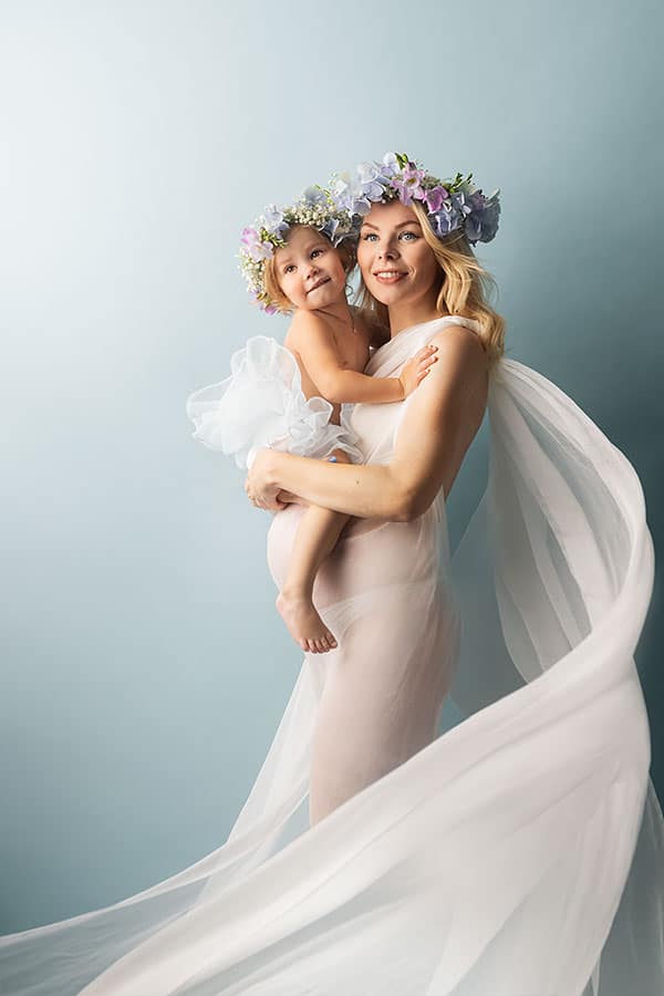 Elegant gravidfotografering av mor og barn med blomsterkrans, perfekt for gravidfoto shoots i Norge. Tidløse bilder som fanger kjærligheten og forventningene til det kommende barnet.