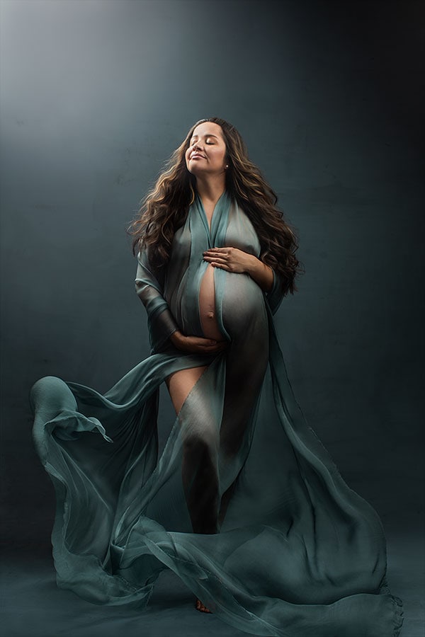 Kvinnelig gravid i elegant gravidfotografering med flytende klær og myk belysning, fremhever den naturlige skjønnheten til den gravide kroppen.