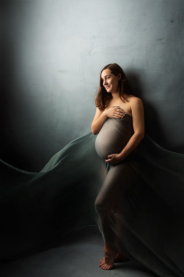 Lysbilde av gravide kvinne i studio, gravidfotografering for gravidefoto, kunstnerisk gravidbilde med rolig uttrykk, profesjonell gravidfotografering av fremtidig mor, gravidfoto som fremhever graviditetens skjønnhet og forventning.