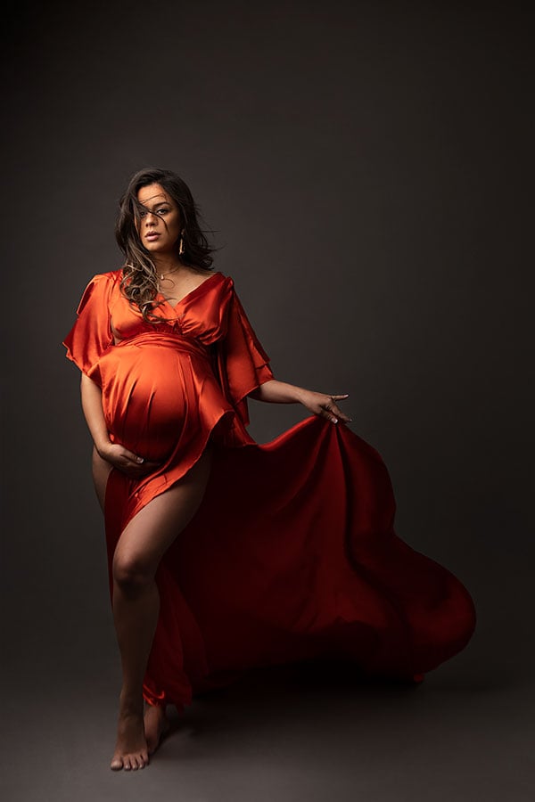 Elegant gravidfotografering av gravide kvinner i studio med rødt plagg og mørk bakgrunn. Fokus på svangerskap, kvinneportrett, gravidfoto, kunstnerisk gravidbilder, profesjonell gravidfotografering.