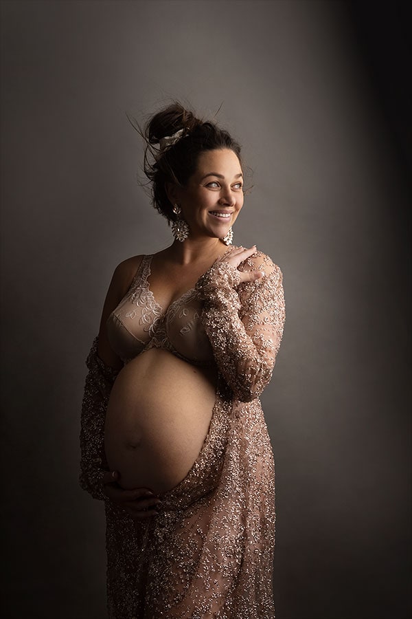 Elegant gravidfoto av smilende, gravid kvinne i vakker nattskjorte, perfekt for gravidfotografering, fokus på livmoren, graviditetssikker fotografering, naturlig gravidopinspirasjon, gravidebilder, gravidfoto stue.