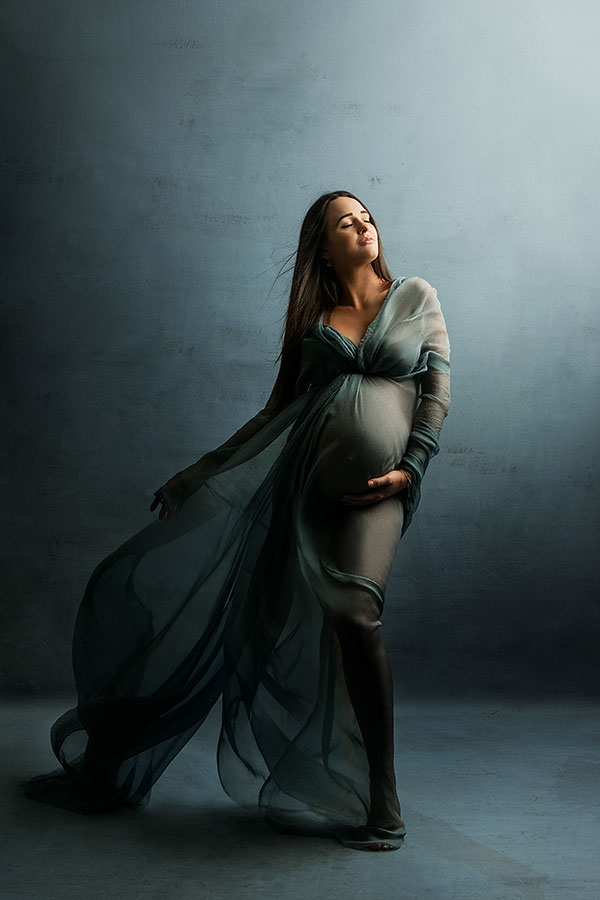 Elegant gravidfoto av kvinne med lang, flowy kjole som fremhever gravid mage, foto for gravidfotografering, kunstnerisk gravidbilde i studio.