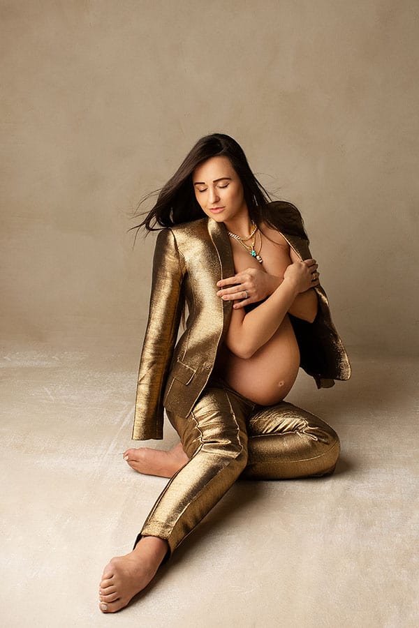 Kvinne som poserer gravidfotografering i gullfarget kostyme, vekt på skjønnheten i graviditet, kunstnerisk gravidfotografering, elegant gravidfoto, kreativ gravidbildestil.