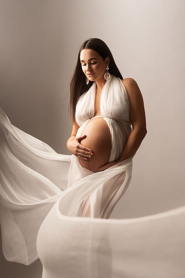 Kvinne som viser gravid mage i elegant hvit gravidfotografering, fokus på kvinne, graviditet, morskap og inspirasjon for gravide.