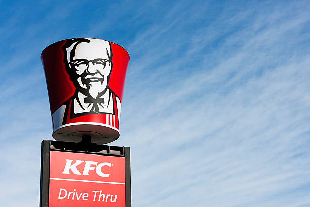 لافتة مطعم KFC كنتاكي فرايد تشيكن مع صورة هارلاند ساندرز وخدمة السيارات في الخلفية