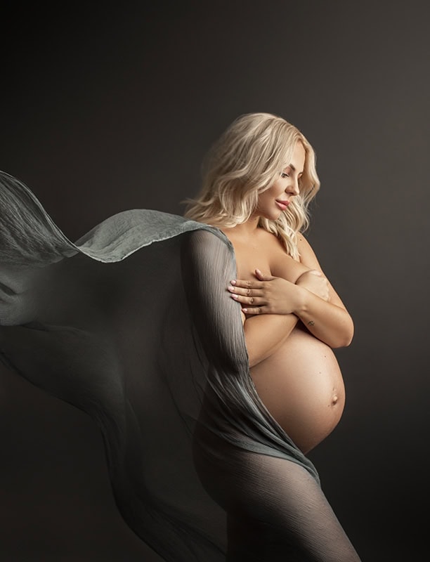 Elegant gravidfotografering av gravid kvinne med chiffonklut som dekker bryst og mage, med mykt lyssetting og enkel bakgrunn. Perfekt for minneverdige gravidbilder og mødrefoto.