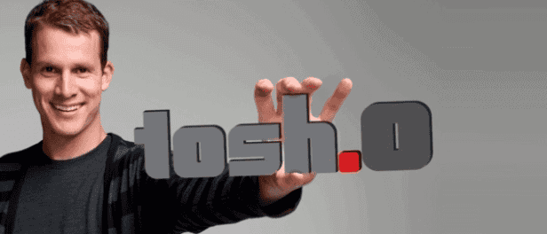 Man holding a "tosh.0" sign with a mechanical bull in the background.