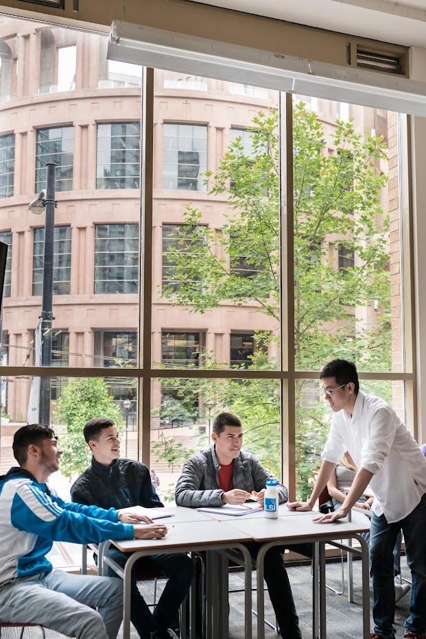 Lehrer und Schüler im interaktiven Sprachunterricht mit großem Fensterblick auf die Vancouver Public Library.