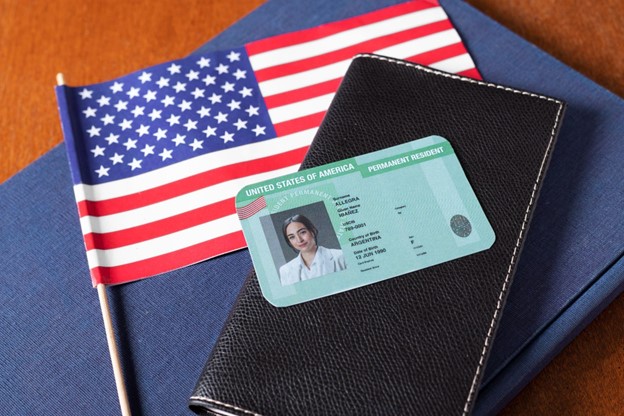 A Permanent Resident Green Card on a black leather wallet next to a small American flag.