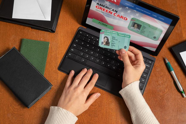 A person holding a Green Card while using a laptop to apply for a replacement online.