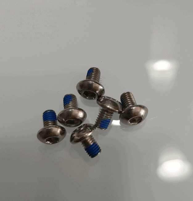 Set of small metal bolts with blue thread lock on a reflective surface.