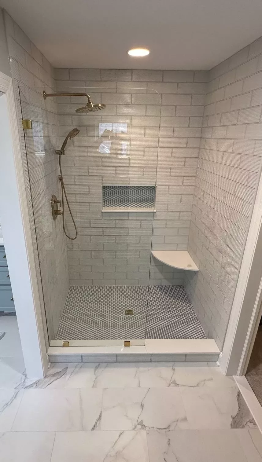 Tile shower with a glass panel, rainfall showerhead, niche, and bench.