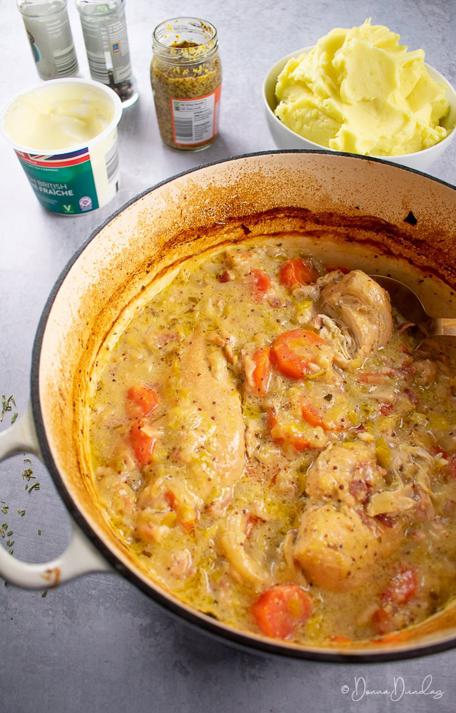 3/4 shot of chicken and cider casserole in cast iron cooking dish, mash and other ingredients in background