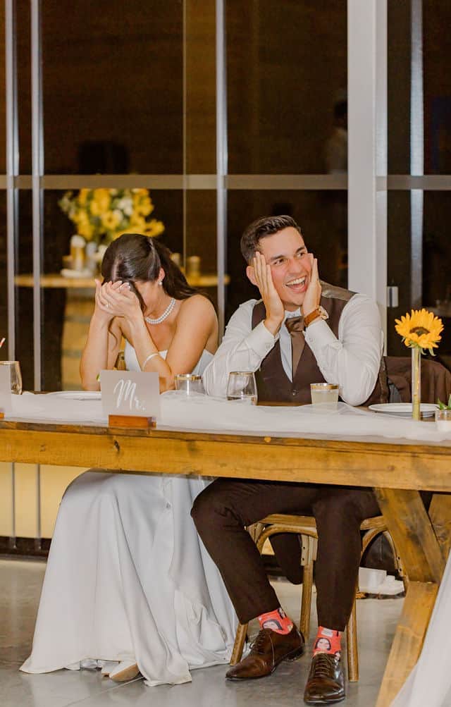 Julia and Will reacting with laughter at the head table during wedding speeches