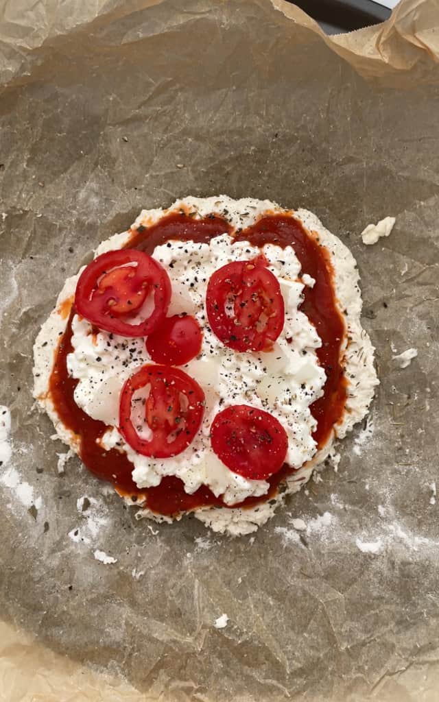 Placing tomatoes on top of the high protein pizza. 