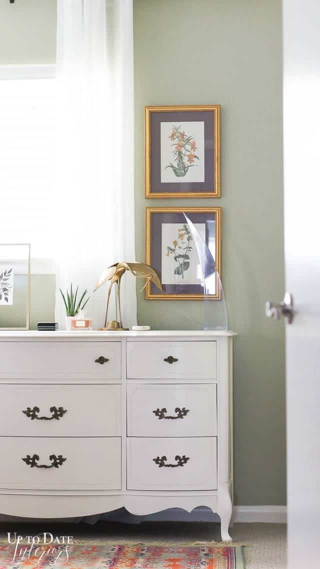 view into bedroom with part of a white dresser and eclectic decor on a green wall and partial window.