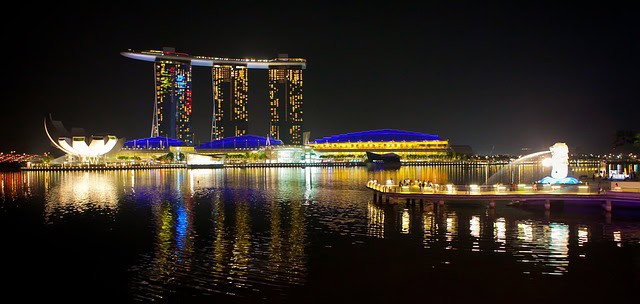 Night view of Marina Bay Sands and Singapore skyline with illuminated buildings reflected on water.