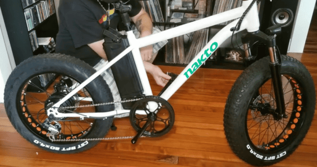 Nakto fat-tire electric bike being assembled indoors, showing battery mounted on the frame and 20x4.0 CST tires.