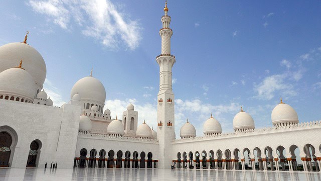 Beautiful white mosque with multiple domes and a tall minaret under a blue sky.