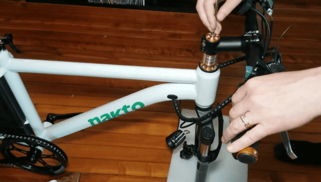 Person assembling a Nakto electric bike by tightening the handlebar stem bolts during setup.