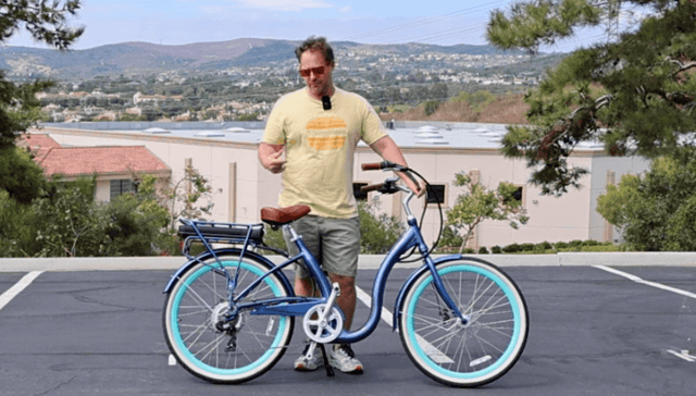 Man standing beside a blue beach cruiser electric bike in a parking lot