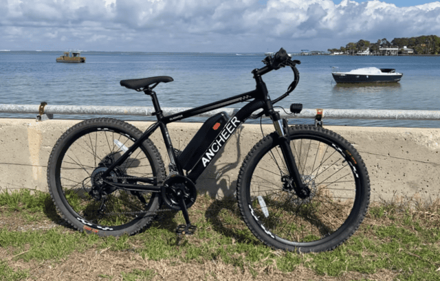 Ancheer Gladiator electric bike by the bay, showing removable downtube battery, hub motor, and mechanical disc brakes