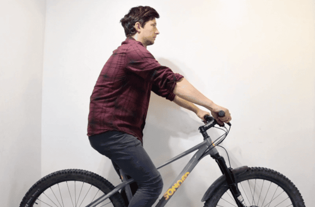 Cyclist in profile checking riding posture with hands on mountain bike handlebars.