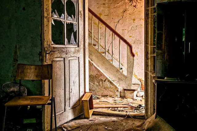 Verfallenes Interieur bei einer Stadtführung Freiburg: Ein alter Stuhl vor einer kaputten Tür mit Blick auf eine Treppe in einem verlassenen Haus.