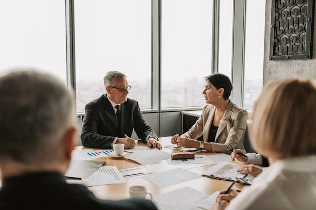Business man and Business woman in a boardroom with papers while two other business people are looking at the front