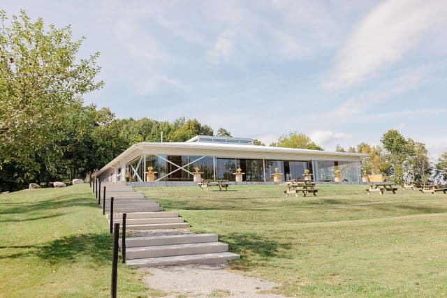 Exterior of the 1818 Farm and Cidery building with patio tables and a path leading up from the lawn