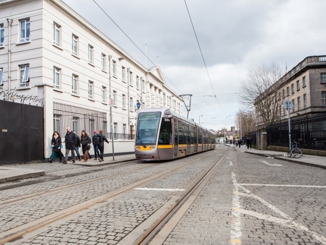 Eine moderne Luas-Straßenbahn fährt auf den gepflasterten Gleisen durch die Straßen von Dublin, während Fußgänger vorbeigehen.