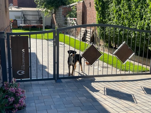 Ein modernes, anthrazitfarbenes Gartentor mit 'Willkommen'-Schild und einem passenden Zaunelement mit zwei Rautendekorationen, präsentiert von Tore & Torsysteme von Stahl- und Metallbau Drost.